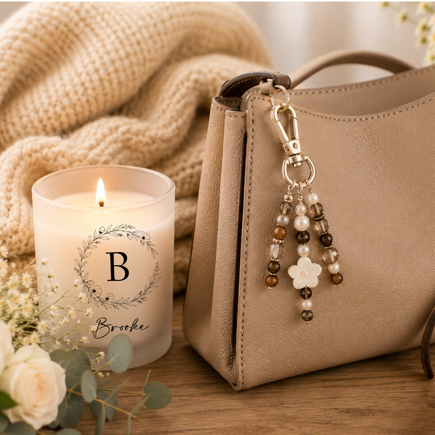 Beige handbag with a beaded keychain next to a lit candle with name on a wooden surface.